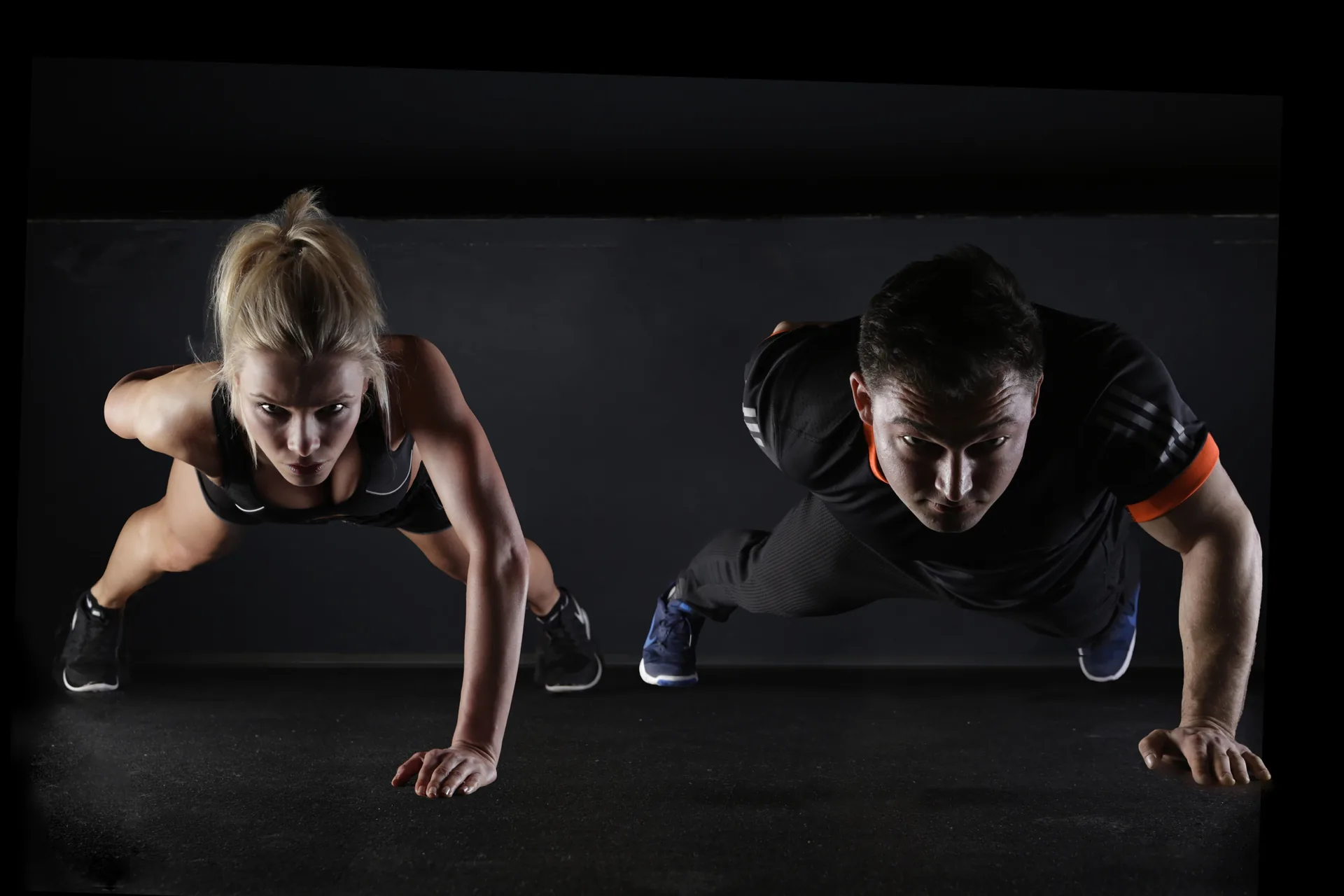 Two athletes performing push-ups together in a dark gym